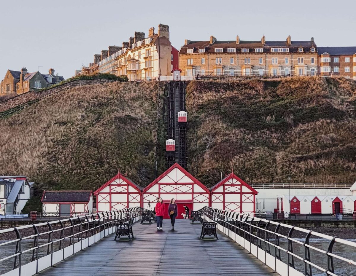 People walking along the Saltburn by the Sea pier beneath the cliff lift