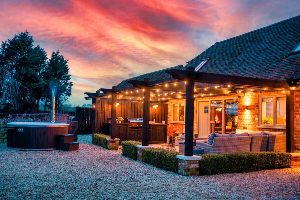 The Coach House at Mount Pleasant Barns at sunset with wood-fired hot tub, pergola and fairy lights, Walton, Warwickshire