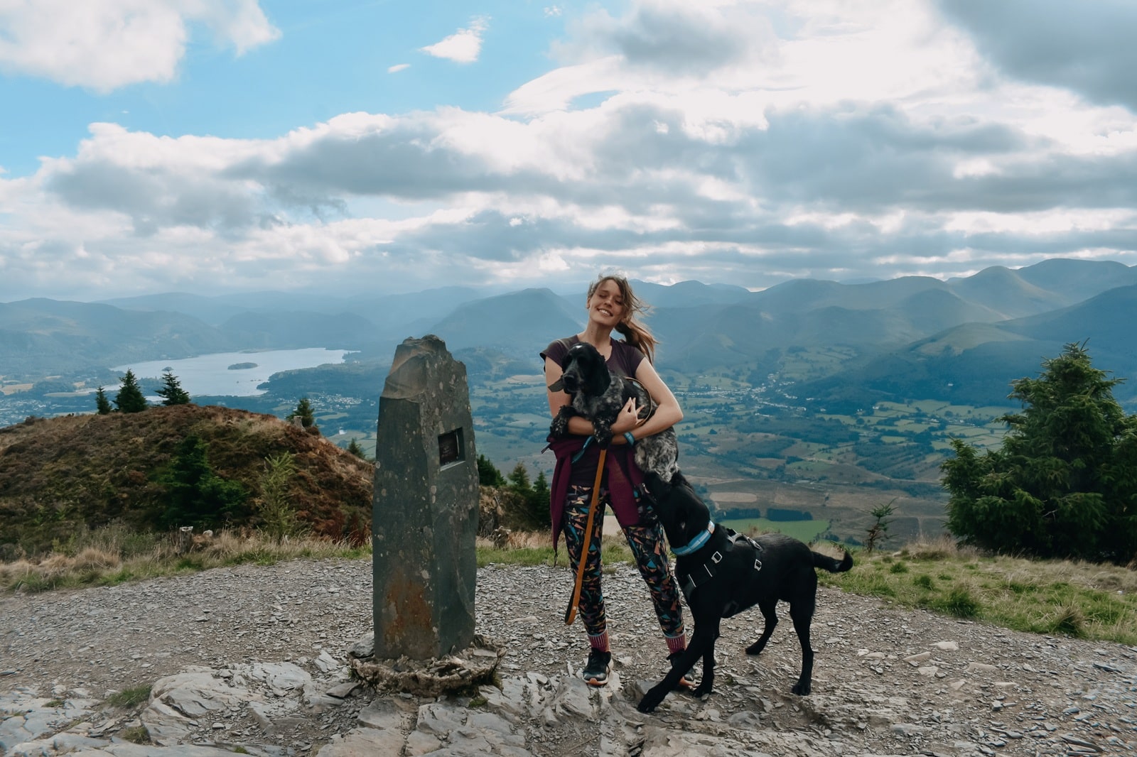 Emma standing with dogs Merry and Coal overlooking the mountain views at Dodd Wood in the Lake District