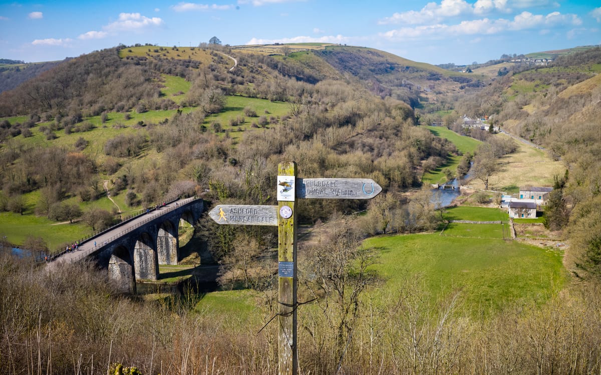 Monsal Head viaduct and wooden signpost in the Peak District with green hills and Monsal Dale below