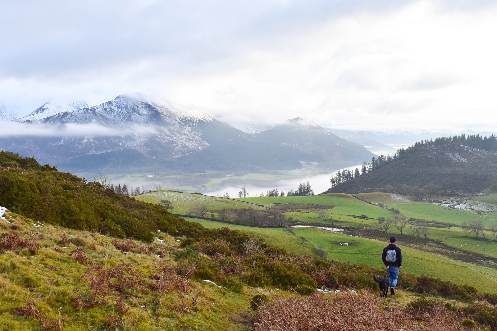 Man and dog trekking through snow-covered scenery on the Sale Fell trail