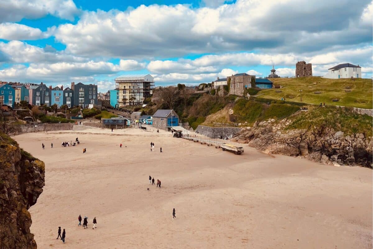 Walkers and dogs on Castle Beach in Tenby, below the lifeboat station and the ruins on Castle Hill