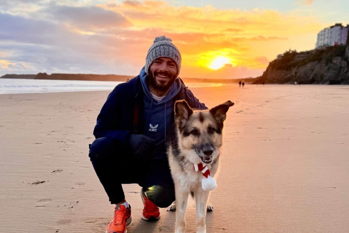 Matt and his German Shepherd Ice on the sand at Tenby at sunset, with the cliffs and town above the beach